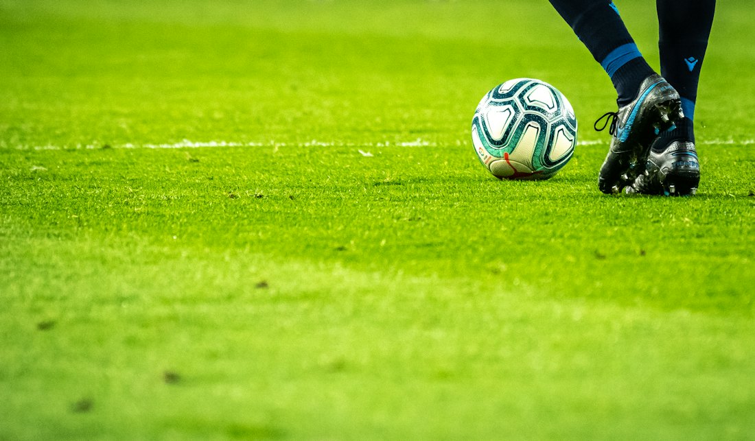 Bola de futebol no gramado, junto à chuteira de um jogador